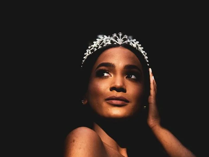 A woman in a yellow gown and jeweled headpiece, her face lit against a dark background.